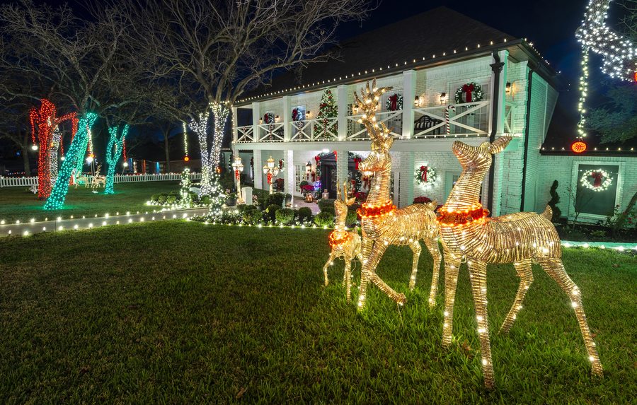 Large two-story home with full Christmas light display, lit reindeer and colored tree wraps