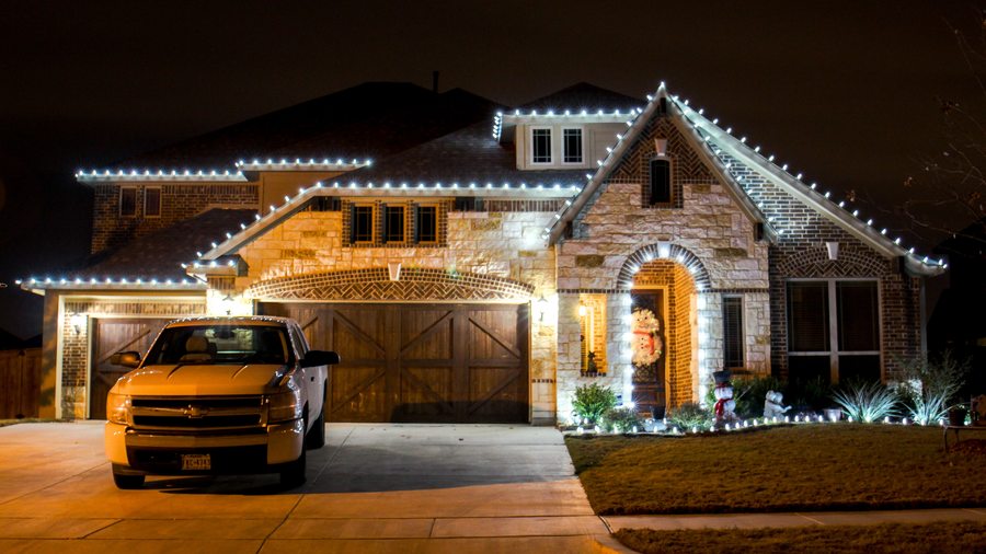 Stone and brick home with cool white roofline Christmas lights and lawn accent lights at night