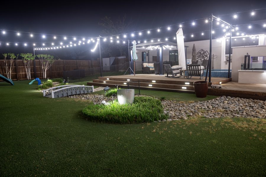 Backyard string lighting with landscape accent lights and deck steps at night