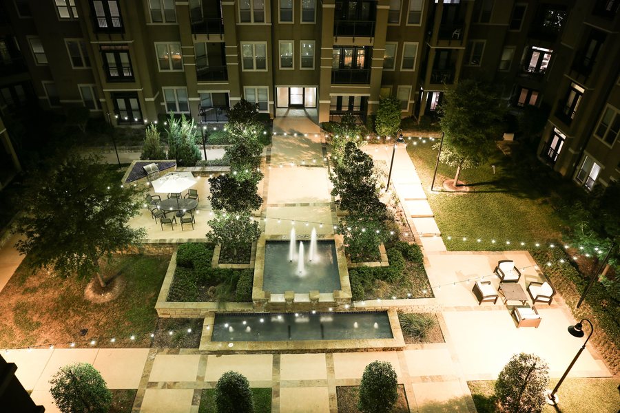 Aerial view of apartment courtyard at night with string lights, fountains and outdoor seating